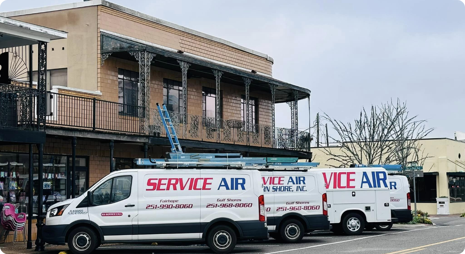 Service Air tech vehicles outside a business that has a balcony -- blue ladder leaning out outside of balcony