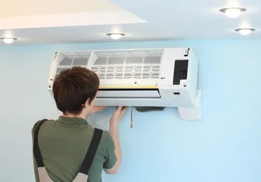 person in green shirt working on a split HVAC unit on a blue wall