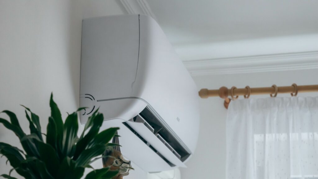 A white wall-mounted air conditioner is installed above a plant near a window with a sheer curtain and a curtain rod. ac freezing up