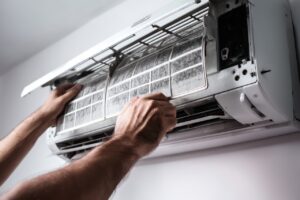 Person removing or cleaning the air filter from a wall-mounted air conditioning unit. Residential AC Replacement